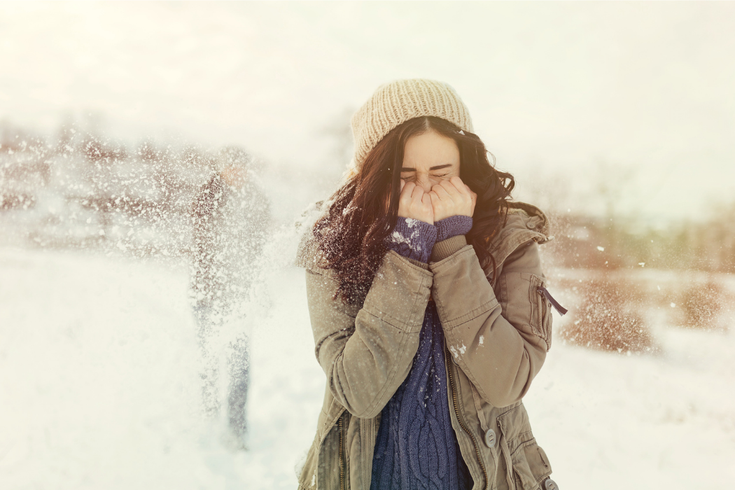 Donna con cappello e giacca pesante che si copre il viso dal freddo e dalla neve, simbolo della necessità di rafforzare le difese immunitarie nei primi freddi
